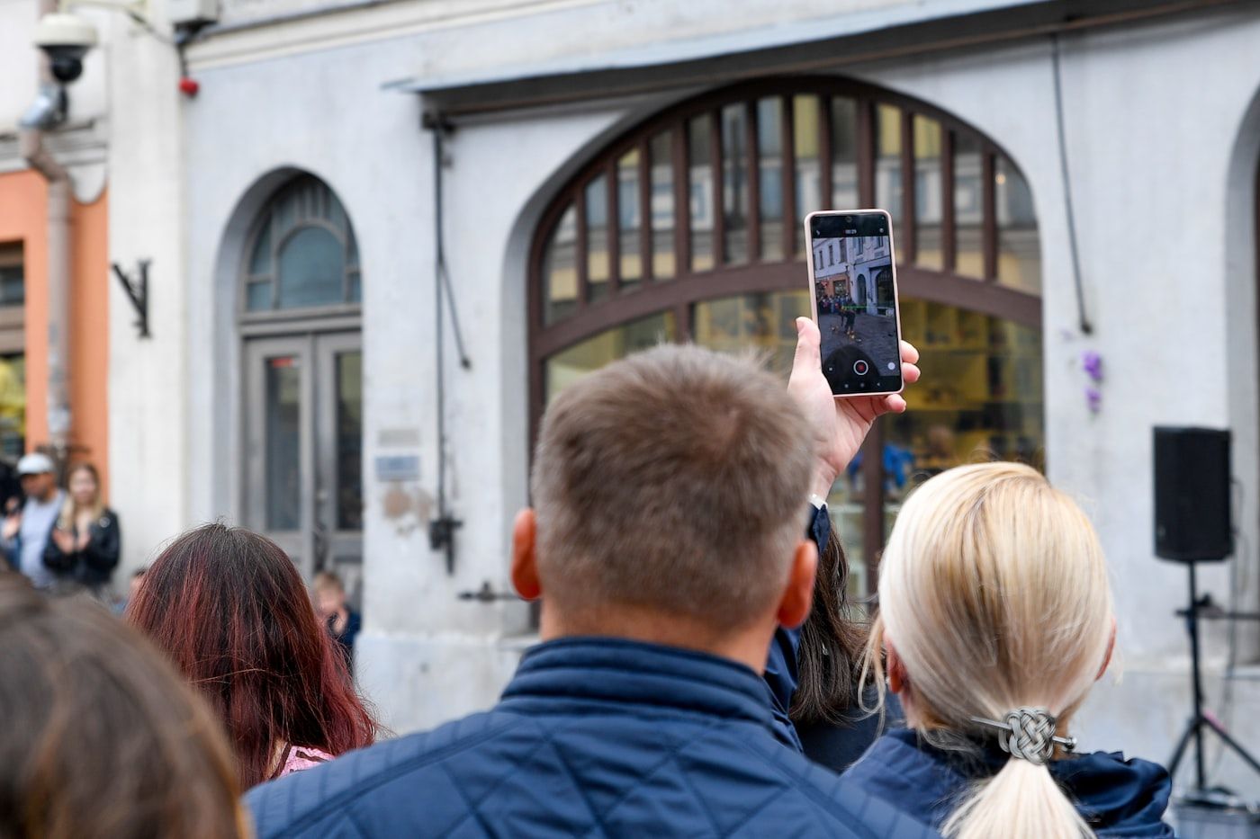 A crowd watching a street performance, one person holding a phone above their heads to film it.