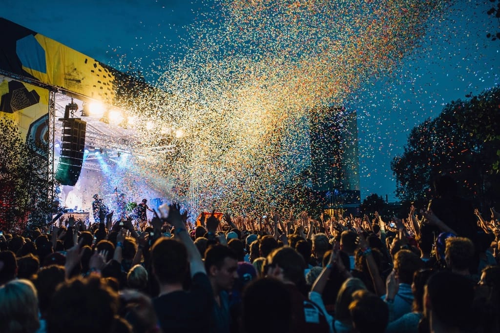A dense night-time festival crowd facing a lit stage as confetti falls.