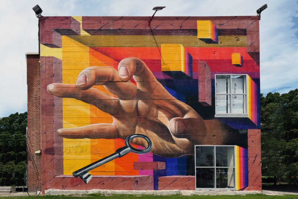 A large, vividly coloured mural of a hand holding a key, painted across the side of a building.