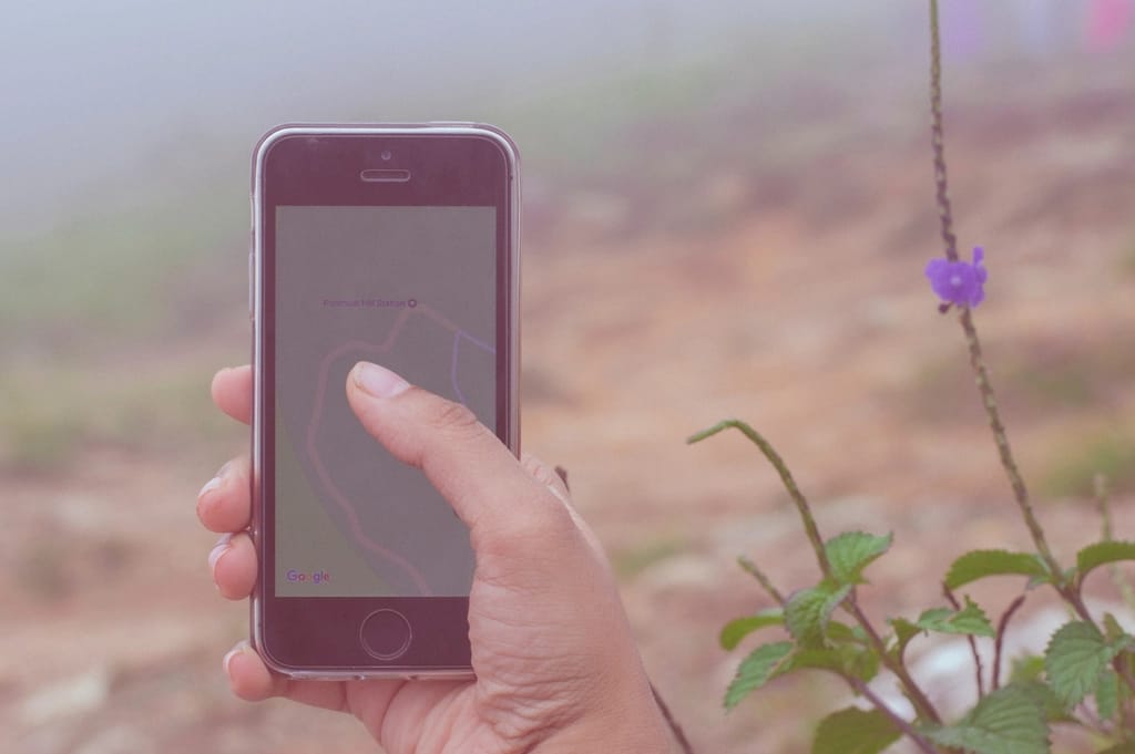 A hand holds a phone showing a map with a route drawn to a destination.