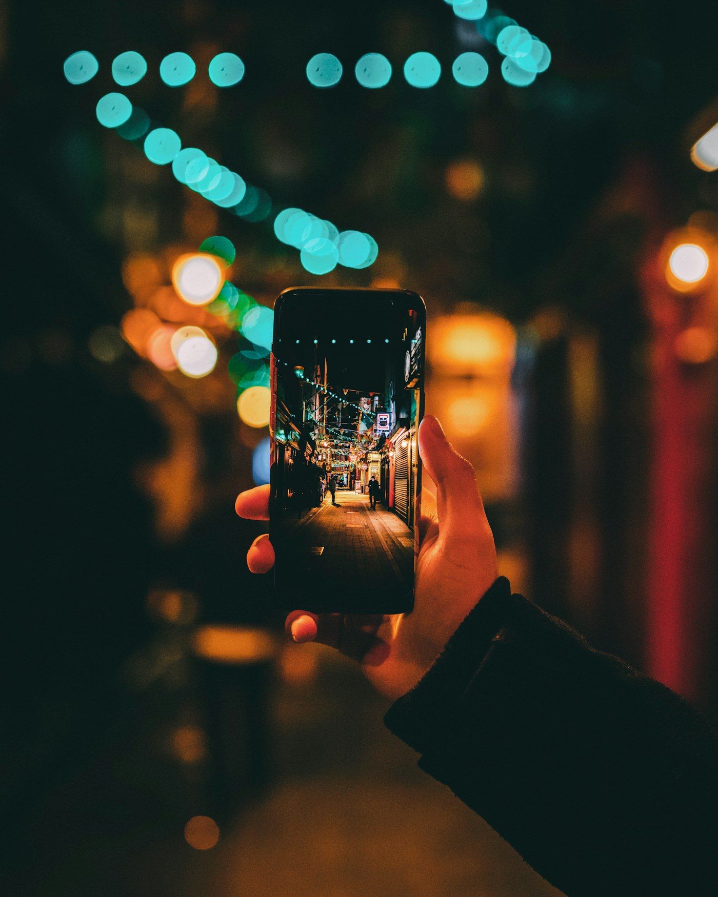 A hand holding up a phone on a lit street at night, the screen showing the street ahead in sharp focus while the scene behind it falls away.