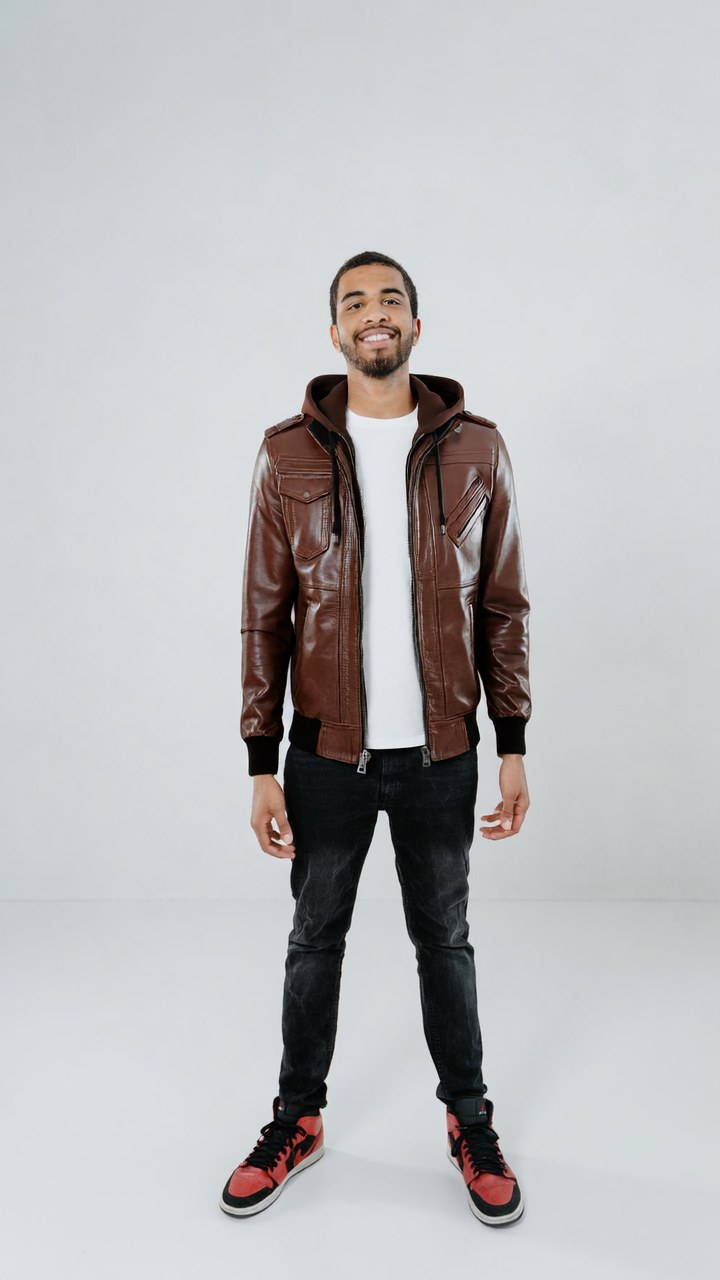 AI try-on: the catalogue's brown leather hooded bomber rendered onto a model standing in a studio.