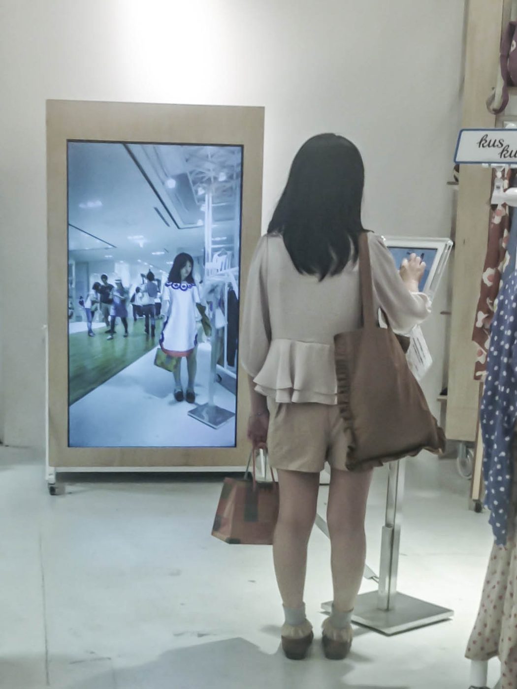 A shopper standing at a virtual try-on mirror in a clothing store. Photo: Ikusuki, CC BY 2.0.