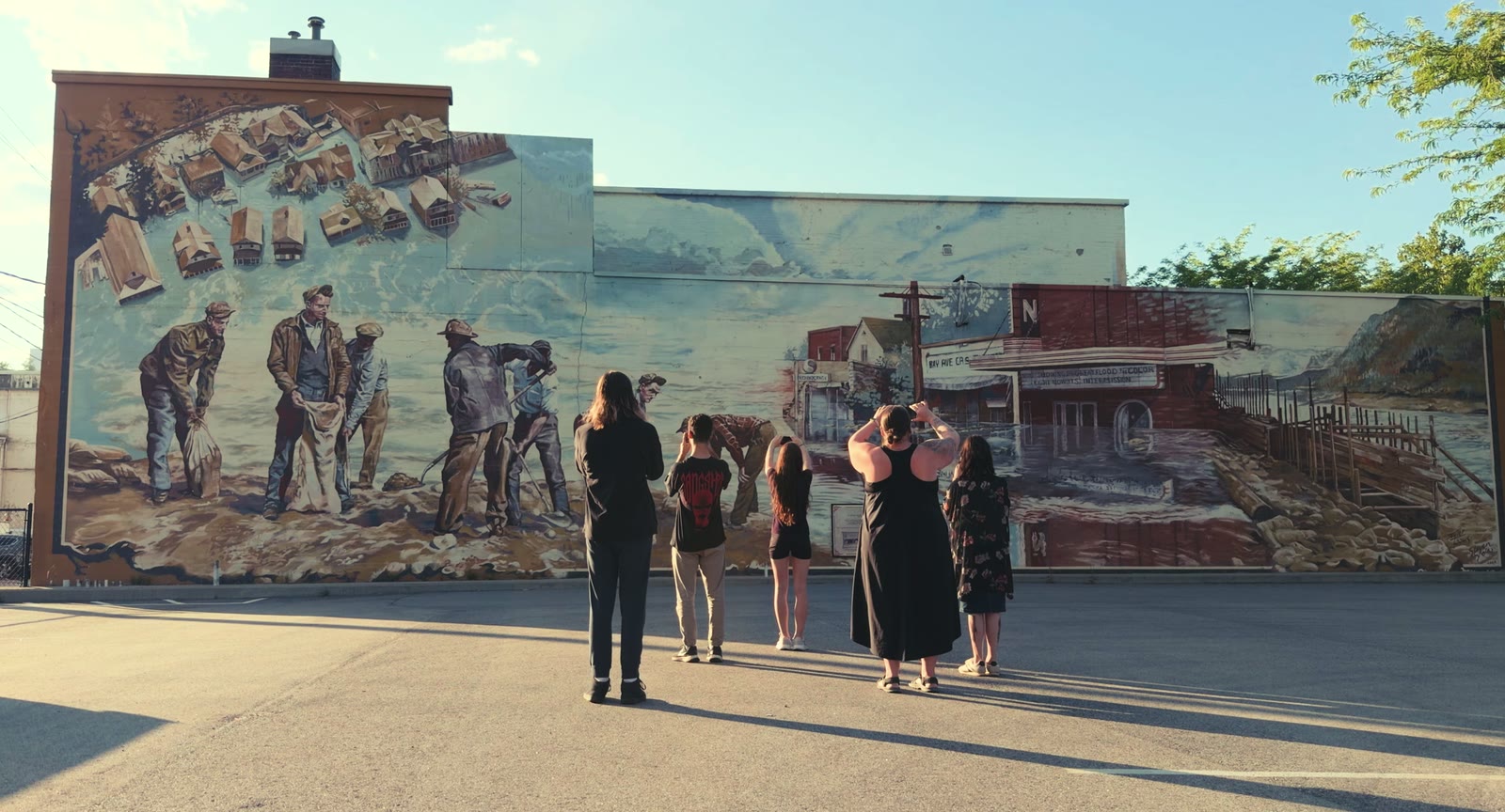 A group of visitors standing in the parking lot in front of Trail's flood mural, phones raised, filming the AR experience.